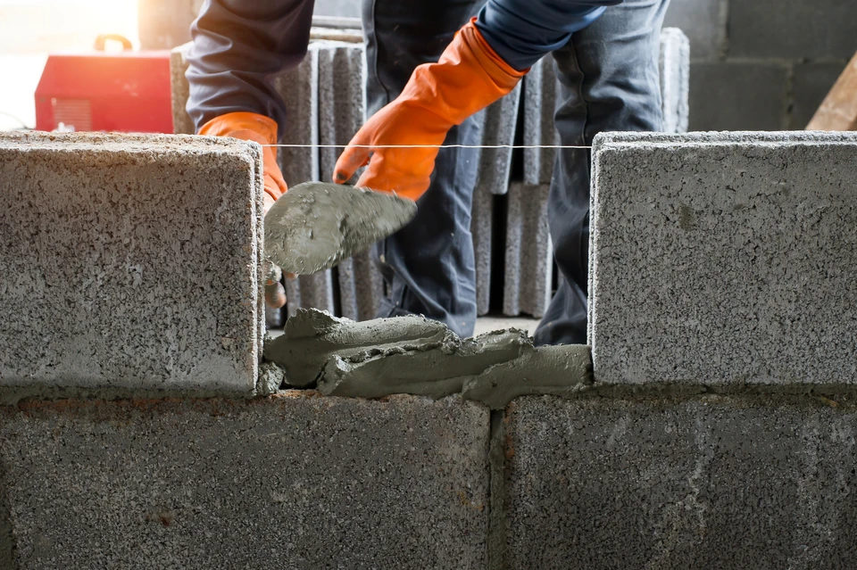 un ouvrier en maçonnerie fait un mur de béton par bloc de ciment et un plâtre sur le chantier
