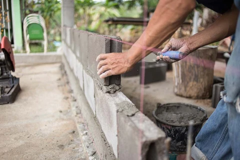 Scène extérieure de construction où un maçon applique du mortier sur un mur en parpaings à l'aide d'une truelle