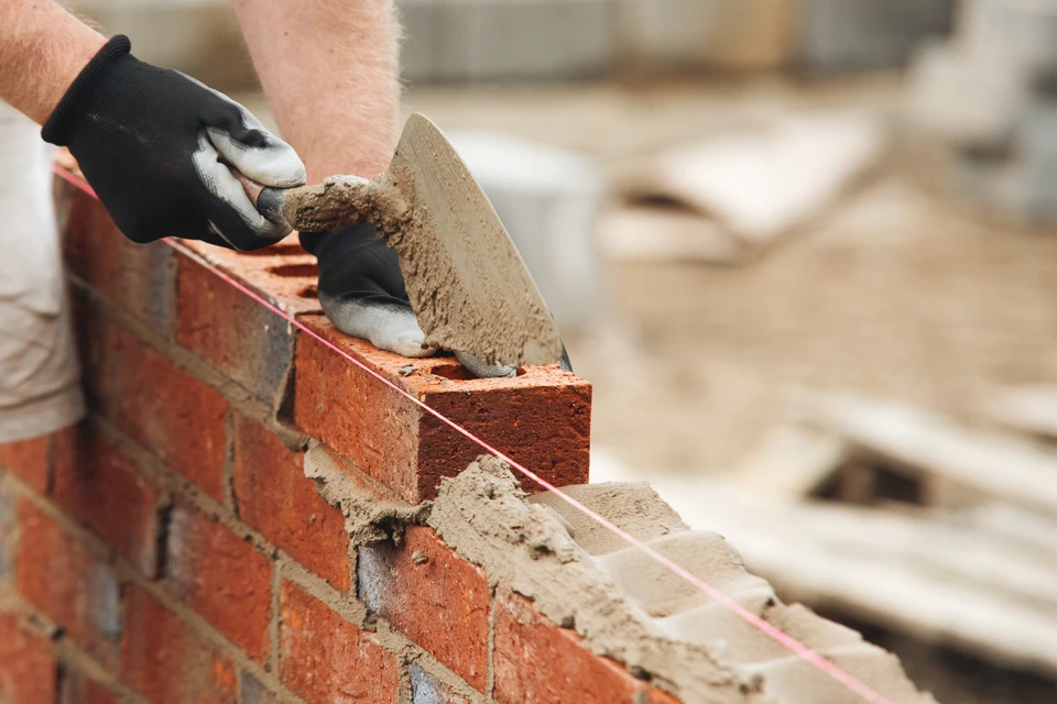 Chantier de construction extérieur avec maçon appliquant mortier sur briques alvéolaires rouges