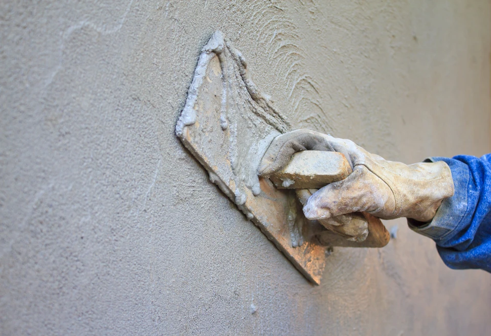 Ouvrier appliquant un enduit de façade sur mur extérieur avec taloche, travaillant en plein air sous lumière naturelle